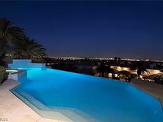 an empty swimming pool at night with the city lights in the background