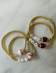 - Fun gold beaded baseball or football 18k gold filled beaded bracelets. Adorned with ceramic sports balls solo or in addition to jersey number. Support your favorite player with these sports bracelet. Gold filled beads are much more tarnish resistant and long lasting, opposed the the more commonly seen gold plated. These bracelets layer well with others so add this to your stack! Beaded on high quality stretch cord and secured. -  4mm 18k gold filled beads      15mm ceramic sports ball bead Sporty Beaded Bracelets For Sports Events, Sporty White Jewelry For Game Day, Sporty Jewelry For Baseball Season Game Day, Sporty Bracelets With Round Beads For Sports Events, Adjustable Gold Beaded Bracelets For Game Day, Sporty Jewelry For Baseball Game Day, Sporty Jewelry For Baseball Season, Baseball Mom Bracelet, Football Mom Gifts