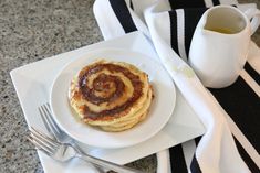 a white plate topped with cinnamon rolls next to a cup of coffee and a fork