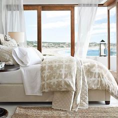 a bed with white sheets and pillows in front of a window overlooking the ocean on a sunny day