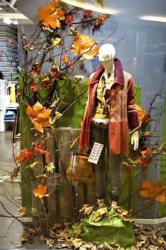 a mannequin dressed in autumn clothing next to a tree with leaves on it