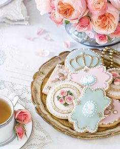 decorated cookies and tea on a tray with pink roses in the background, next to a cup of tea