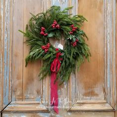 a christmas wreath hanging on the front door with red ribbon and mistlet berries in it