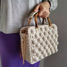 a woman is holding a crocheted bag with chains on the handle and handles