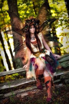 a woman dressed as a fairy sitting on a bench in the woods with her wings spread