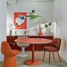 an orange chair sits in front of a round table with two chairs and a painting on the wall behind it