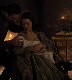 a man holding a baby next to a woman in a dress and candle lit room