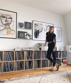 a woman standing in front of a wall with records on it and pictures above her