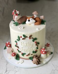 a baby shower cake decorated with woodland animals and mushrooms on a marble table top,