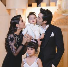 a man and woman holding a baby in front of two other people wearing formal wear