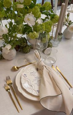 a table set with place settings and flowers in vases on the side, along with napkins