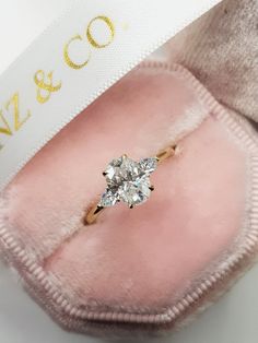 an engagement ring sits on top of a pink velvet case