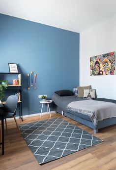 a bedroom with blue walls and wood flooring is pictured in this image, there is a small bed on the far side of the room