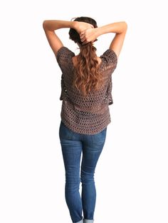 a woman standing with her hands behind her head and looking down at the ground while holding her hair back