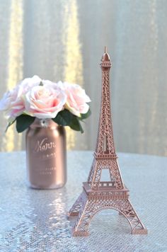 a pink rose sits in front of the eiffel tower on a table next to a jar of flowers