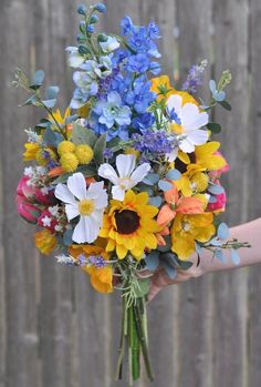 a person holding a bouquet of flowers in their hand with a wooden fence behind them