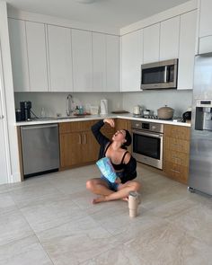 a woman sitting on the floor in front of a stove top oven with a water bottle next to her