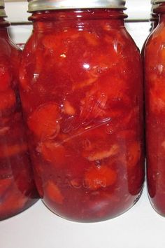 four jars filled with pickled tomatoes sitting on top of a white counter next to each other