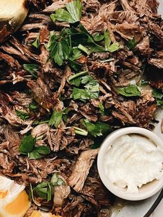 a plate filled with meat and vegetables next to bread on a white tablecloth covered in greens