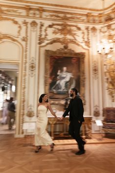 a bride and groom holding hands in an ornate room