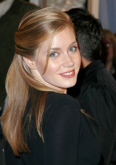 a woman with long hair and blue eyes smiles at the camera while standing next to a man