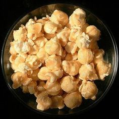 a glass bowl filled with corn kernels sitting on top of a table next to a black background