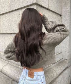 the back of a woman's head with long dark brown hair standing in front of a stone wall