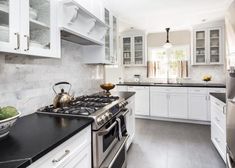 a kitchen with white cabinets and black counter tops is pictured in this image, there are two tea kettles on the stove