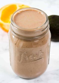 a glass jar filled with smoothie sitting next to an orange and avocado