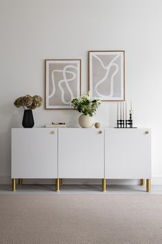 two vases with flowers sit on top of a white cabinet