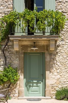 a green door and window in front of a stone building with plants growing on it