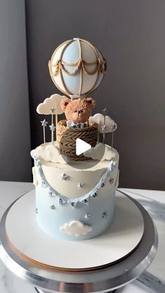 a teddy bear sitting in a basket on top of a white and blue cake with silver trim