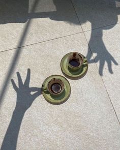 two coffee cups sitting on top of saucers next to each other in front of a person's shadow