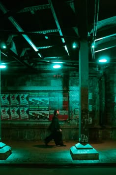 a man walking down a street at night with green lights on the ceiling and graffiti all over the walls