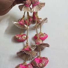 someone is holding up some pink and gold ornaments on a white tablecloth with a hand reaching for the bead