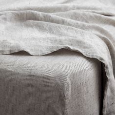 an unmade bed with grey linens and sheets on top of eachother