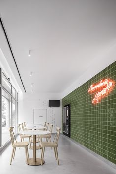 an empty restaurant with green tile walls and wooden chairs around a round table in front of a neon sign on the wall