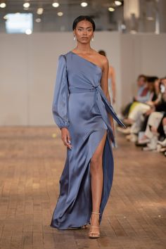 a model walks down the runway in a blue dress with an asymmetrical slit