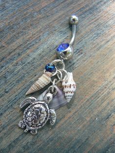 a sea turtle, starfish, and shell charm on a wooden surface with a dangling belly ring