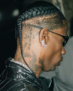 a man with braids and tattoos on his head looking off into the distance while wearing glasses