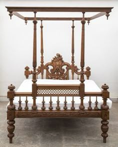 an antique wooden bed with four posts and white sheets on the bottom, against a wall