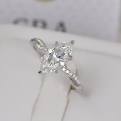 an engagement ring with a pear shaped diamond in the center on a white box,