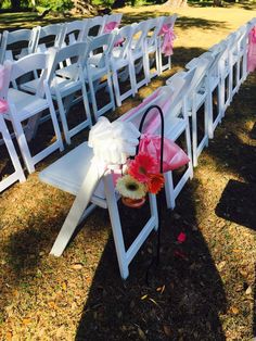 rows of white folding chairs with pink bows and flowers on the seats are set up for an outdoor ceremony