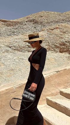 a woman in a black dress and hat walking down some steps with a handbag