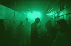 a group of people standing in a dark room with green light coming from the ceiling