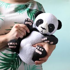 a woman holding a stuffed panda bear in her arms with palm leaves on the background