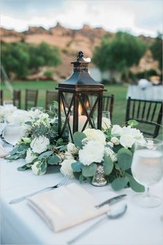 a table with white flowers and greenery is set up for an outdoor wedding reception