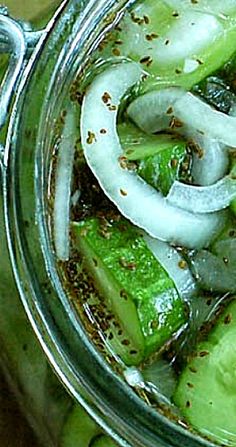 a glass jar filled with sliced cucumbers and seasoning on top of a wooden table