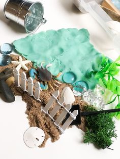 an assortment of sand and seaweed on a white surface with plastic bottles, scissors and other items