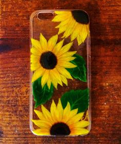 sunflowers painted on the back of a phone case sitting on a wooden table